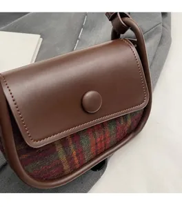Close-up of brown leather saddle bag with plaid fabric detailing and snap button