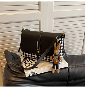 Detail of black leather and houndstooth bag with gold hardware and plush rabbit charm