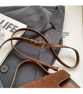 Close-up of adjustable brown shoulder strap with gold metal buckle on a small square bag