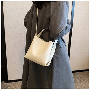 Vista dettagliata di una borsa a secchiello bianco sporco con trama, manico e logo