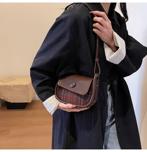 Detail of vintage saddle bag featuring green plaid wool fabric and brown leather flap