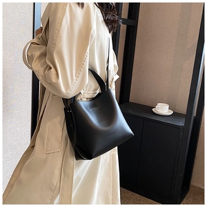 Dettaglio della borsa a secchiello in pelle nera con logo mostrata su una modella in trench