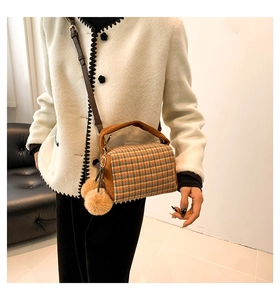 Detailed view of a brown plaid Boston bag with plush pendant on a model in indoor setting