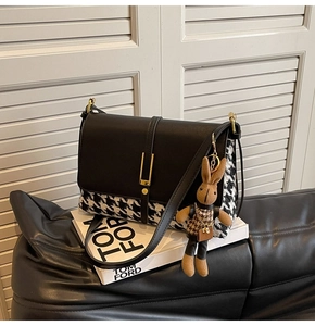 Detail of black leather and houndstooth tote bag with golden metal buckle and cute rabbit charm