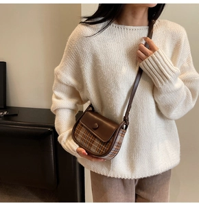Detail of a vintage brown plaid saddle bag worn cross-body with adjustable leather strap