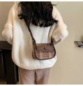 Close-up of brown vintage saddle bag featuring plaid fabric and leather flap details