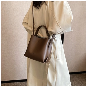 Dettaglio borsa a secchiello in pelle marrone scuro con logo Maighee su trench beige