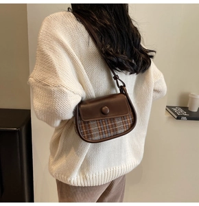 Detail view of small saddle bag with brown leather flap and autumn plaid texture
