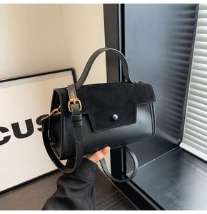 Detail of black crossbody bag with smooth leather and suede patchwork held by model