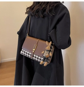 Detail of brown leather and houndstooth crossbody bag with a knit rabbit charm