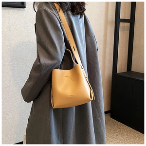Modella che indossa una borsa a secchiello in pelle color cammello con tracolla larga e logo