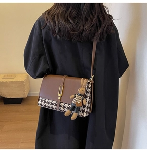 Detail of crossbody bag with houndstooth pattern and a cute brown plush rabbit pendant