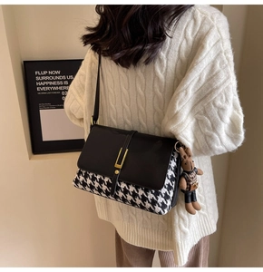 Detail of houndstooth tote bag with black leather flap and gold buckle on sweater
