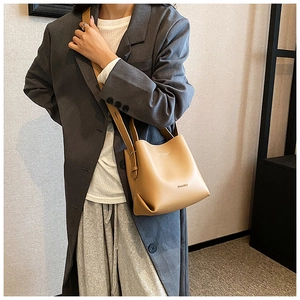 Vista laterale di una borsa a secchiello in pelle marrone chiaro con un blazer grigio