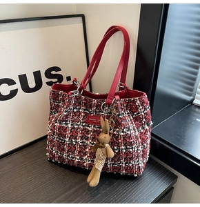Detail of red tweed tote bag featuring leather handles and cute rabbit charm accessory