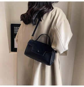 Detail of a black leather crossbody bag with suede flap shown on a shoulder