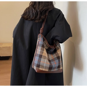 Detail einer großen karierten Beuteltasche mit braunen Lederriemen und Knotendesign am Modell