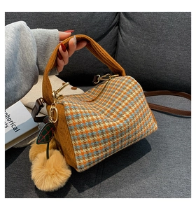 Detail of houndstooth Boston bag with knit handles and a furry pompom charm