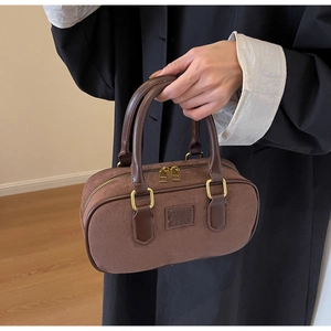 Dettaglio di una borsa cilindrica in pelle scamosciata marrone con manico in pelle