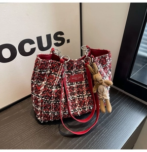 Detail of red and black tweed tote bag with plush bunny charm and leather shoulder strap