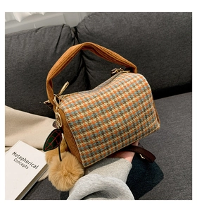 Detail of colorful plaid Boston bag with knitted handle and plush leaf pendant