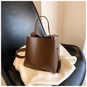 Dettaglio di una borsa a secchiello in pelle opaca marrone scuro con manico e tracolla lunga
