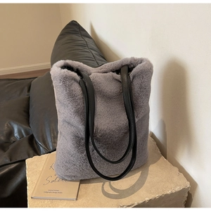 Gros plan d'un sac cabas en peluche grise avec poignées en cuir noir sur pierre