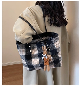 Close-up of vintage plaid tote bag with plush bunny pendant and black leather strap