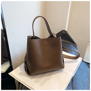 Dettaglio della borsa a secchiello in pelle marrone con logo dorato su sfondo pulito