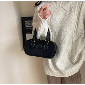 Dettaglio borsa a tracolla nera opaca con finiture dorate indossata con un maglione bianco