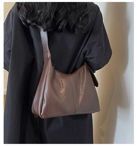 Rear view of a model wearing a large dark brown faux leather tote bag with wide strap