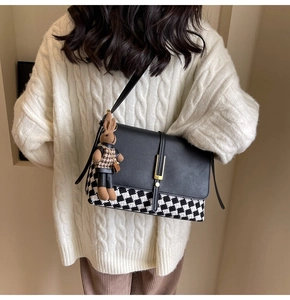 Detail of checkered tote bag with leather flap and rabbit charm worn over a knit sweater
