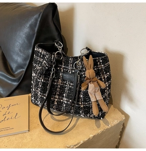 Detailed texture of black and white tweed tote bag with chain strap and bunny charm