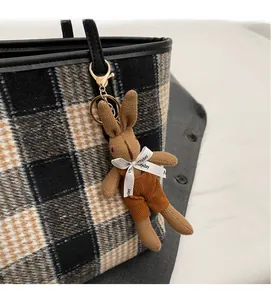 Close-up of a brown knitted bunny charm with orange corduroy overalls on a tote bag