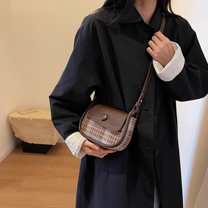 Brown plaid saddle bag with leather flap shown on model in black winter coat