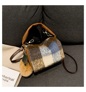 Close-up of plush Boston bag with checkered pattern, pom-pom charm and golden hardware