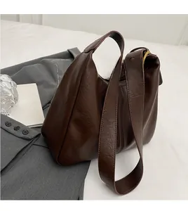 Detail of a dark brown leather hobo bag with wide shoulder strap and gold hardware