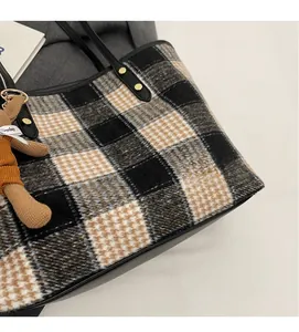 Detail of plaid tote bag fabric with leather trim, rivets and a cute bear charm