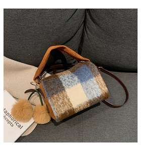 Detail of plaid Boston bag with fuzzy texture and cherry charm on a soft sofa