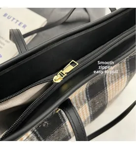 Close-up of smooth golden metal zipper and black leather trim on plaid tote bag