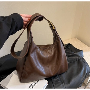 Macro detail of brown leather tote bag showing rich texture and golden metal buckle