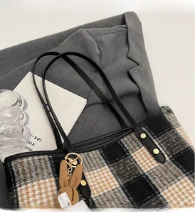 Close-up of plaid tote bag with tweed texture, black leather handle and rabbit charm