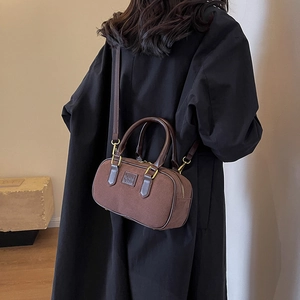 Borsa a cilindro retrò satinata marrone con manici in pelle, indossata dal modello