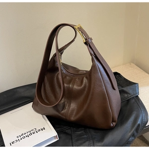 Detail of dark brown leather hobo bag with gold buckle on a stylish black leather backdrop