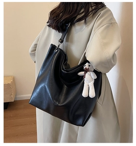 Detail of black faux leather tote with textured finish and cute knit teddy bear charm