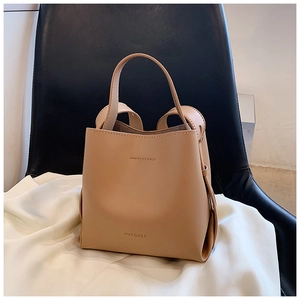 Dettaglio borsa a secchiello in pelle beige con manico e logo del marchio dorato