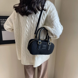 Borsa Boston nera classica con dettagli dorati e manici in pelle su un maglione bianco