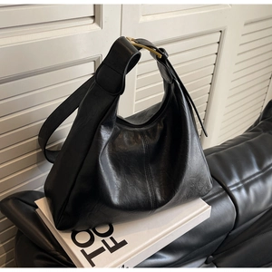 Detail of glossy black leather texture and gold buckle on a large commuter tote bag