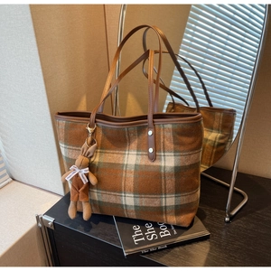 Detail of green plaid tote bag with brown leather straps and plush rabbit charm
