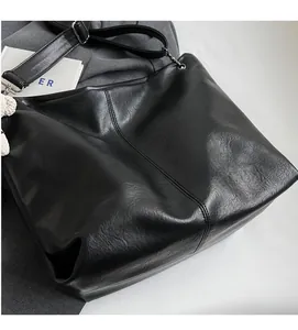 Detail of soft black leather tote bag with vertical stitching and plush bear charm